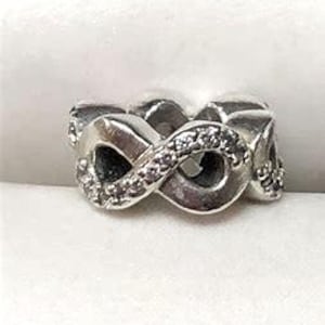 May include: Silver infinity ring with clear cubic zirconia stones. The ring is made of two intertwined bands that form an infinity symbol.