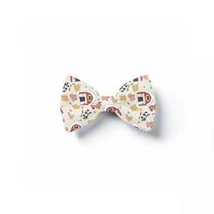 May include: A white bow tie with a farm animal print. The print features red barns, cows, pigs, chickens, and hay bales.