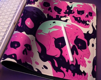 May include: A rectangular desk mat featuring a repeating pattern of pink and black skulls with star-shaped eyes, accompanied by a white mechanical keyboard, a white stylus, and a white wireless earbud charging case on a purple surface.