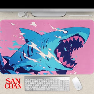 May include: A pink mouse mat with a stylized blue shark design, open-mouthed with sharp teeth. The design includes white and teal accents, with the text "SAN CHAN" in red at the bottom. A keyboard and mouse are visible.