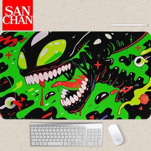 May include: A rectangular mousepad with a striking alien illustration in black, green, and red. The design features a creature with large eyes, sharp teeth, and a long tongue. The mousepad has the text "SAN CHAN" in a red box in the upper left corner.