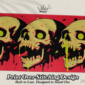 May include: A rectangular mat featuring three stylized skulls with yellow and black details against a red background. The skulls have green eyes and dripping yellow accents. The mat measures 24" x 14".