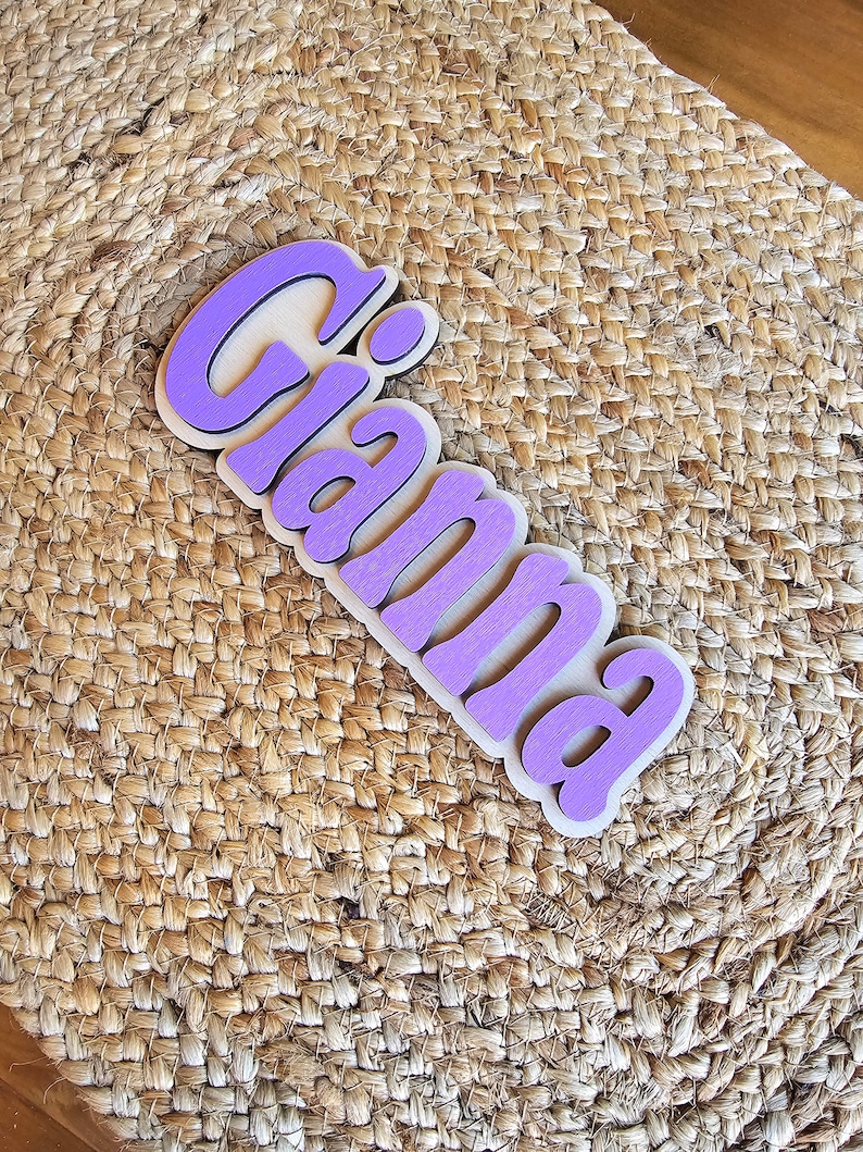 May include: Purple wooden name sign with the name "Gianna" in a stylized font.