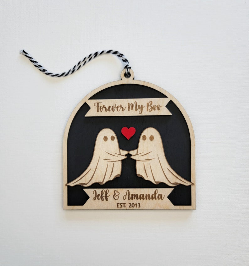 May include: Wooden ornament with two ghosts holding hands and a red heart. The ornament is black with the text "Forever My Boo" and "Jeff & Amanda EST. 2013".