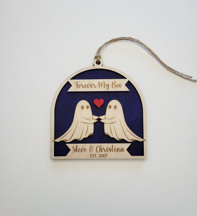 May include: Wooden ornament with two ghosts holding hands and a red heart. The ornament is painted blue and has the text "Forever My Boo" and "Steve & Christina EST. 2007".