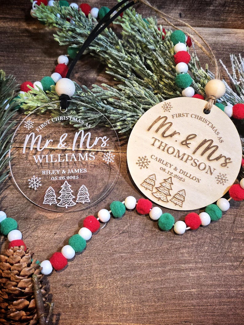 May include: Two Christmas ornaments with the text "First Christmas as Mr. & Mrs." One is clear acrylic, the other wood. The clear ornament says "Williams" and the wooden one says "Thompson". Both have names and dates. A garland with red, white, and green beads is in the image.