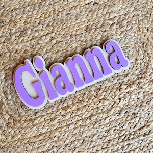 May include: Purple wooden sign with the name "Gianna" in white letters.