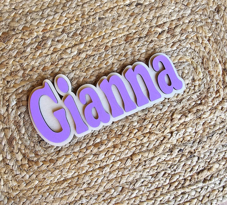 May include: Purple wooden sign with the name "Gianna" in white letters.