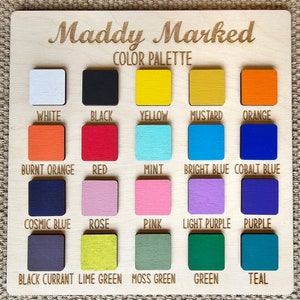 May include: A wooden color palette labeled "Maddy Marked" with 20 square color swatches. Colors include white, black, yellow, mustard, orange, burnt orange, red, mint, bright blue, cobalt blue, cosmic blue, rose, pink, light purple, purple, black currant, lime green, moss green, green, and teal.