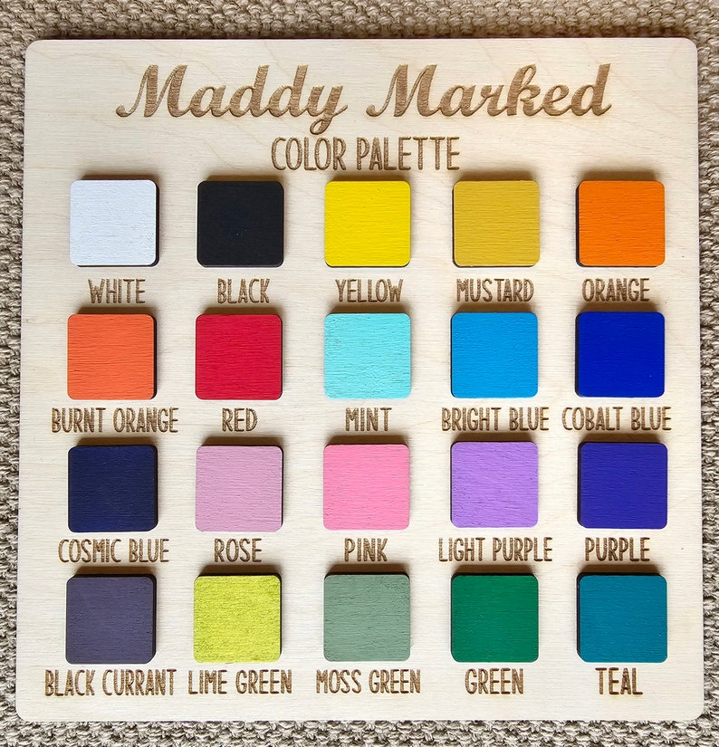 May include: A wooden color palette labeled "Maddy Marked" with 20 square color swatches. Colors include white, black, yellow, mustard, orange, burnt orange, red, mint, bright blue, cobalt blue, cosmic blue, rose, pink, light purple, purple, black currant, lime green, moss green, green, and teal.