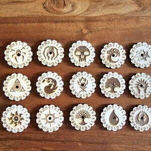 May include: Set of 16 wooden dice with different symbols and numbers. Each die has a unique design, including a spider, skull, tree, and sun.