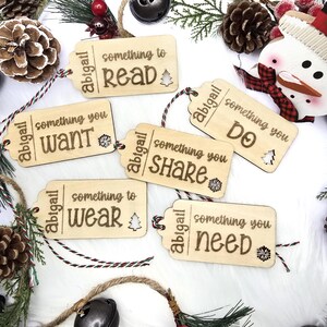 Pu&ograve; includere: Sei etichette regalo in legno con uno spago rosso e bianco. Ogni etichetta ha il nome "Abigail" e una frase diversa: "qualcosa da leggere", "qualcosa che vuoi", "qualcosa da indossare", "qualcosa da condividere", "qualcosa da fare" e "qualcosa di cui hai bisogno".