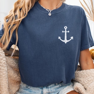 May include: Denim blue t-shirt with a white anchor graphic. The shirt is short-sleeved and has a relaxed fit. The model is wearing denim shorts and a cream-colored sweater. The word "Denim" is printed at the top of the image.