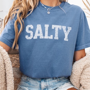 May include: A blue t-shirt with the word "SALTY" printed in white on the front. The shirt is made of a soft, comfortable material and has a relaxed fit.