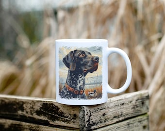 Könnte beinhalten: Weiße Keramiktasse mit einer bunten Illustration eines Deutsch Kurzhaar Hundes in einer Jagdszene. Der Hund schaut nach rechts und hat ein braunes und schwarzes Fell.