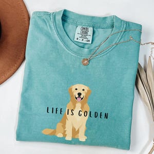 May include: A teal blue t-shirt with a graphic of a golden retriever and the text "Life is Golden".