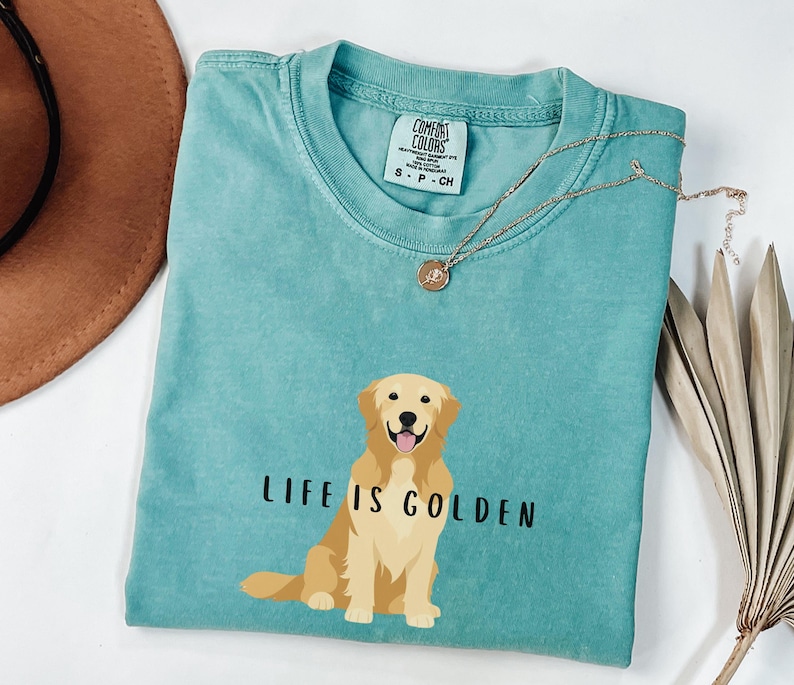May include: A teal blue t-shirt with a graphic of a golden retriever and the text "Life is Golden".