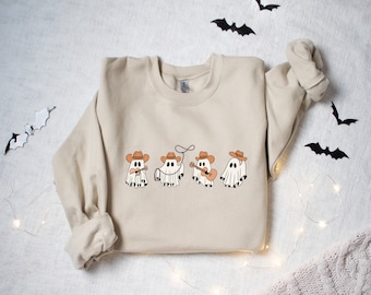 May include: A beige sweatshirt with a graphic of four ghosts dressed as cowboys. The ghosts are wearing brown cowboy hats and are playing musical instruments.