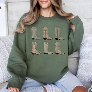 May include: A green sweatshirt with a pattern of six brown cowboy boots with floral embroidery.