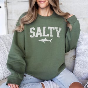 May include: A green sweatshirt with the word "SALTY" printed in white with a white shark silhouette underneath.