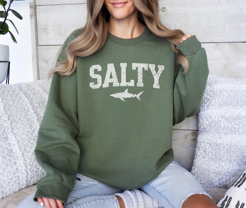 May include: A green sweatshirt with the word "SALTY" printed in white with a white shark silhouette underneath.