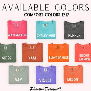 May include: A selection of 12 folded t-shirts in various colors, including watermelon, chalky mint, pepper, moss, yam, burnt orange, bright salmon, bay, violet, and melon. The text "AVAILABLE COLORS" and "COMFORT COLORS 1717" is displayed above the shirts.