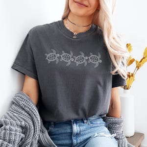May include: A dark gray t-shirt with a white outline of five sea turtles in a row.