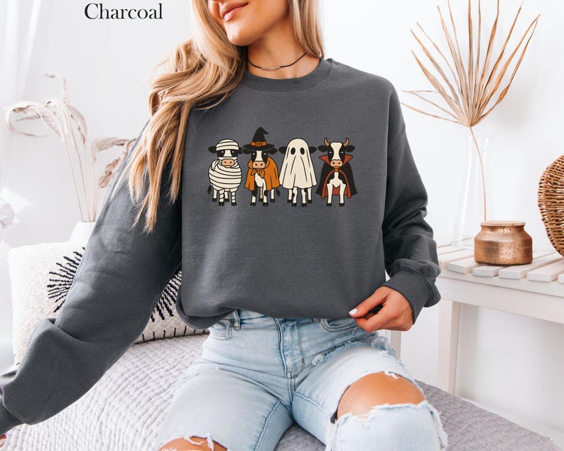May include: Charcoal-colored sweatshirt featuring a Halloween-themed graphic of four cows dressed as a mummy, witch, ghost, and vampire. The sweatshirt is a dark gray color and has long sleeves. The word "Charcoal" is printed at the top.