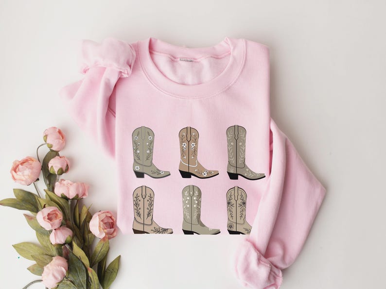May include: Pink sweatshirt with a graphic of six brown cowboy boots with floral embroidery.