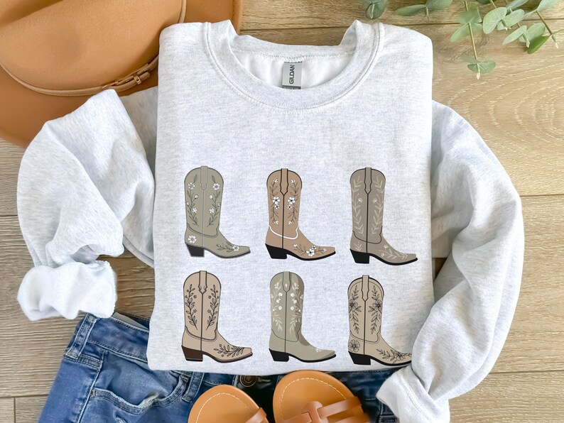 May include: A gray sweatshirt with a graphic of six brown cowboy boots with floral embroidery. The boots are arranged in two rows of three.