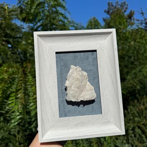 May include: A white crystal rock framed in a white wood frame with a blue fabric mat.