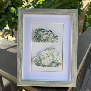 May include: A framed artwork featuring two green and white agate stone clouds. The clouds are displayed on a white background with a light gray mat.