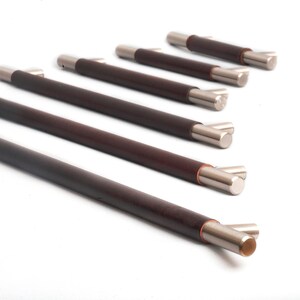 May include: A set of six cabinet pulls. Each pull features a dark brown, cylindrical handle with silver-toned metal end caps. The pulls are arranged diagonally against a white background, showcasing their design and finish.
