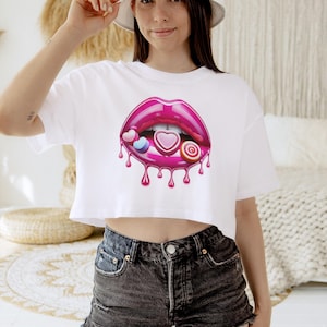 May include: White cropped t-shirt with a pink, glossy, dripping lips design. The lips are filled with colorful candy hearts and a swirl lollipop.