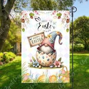 May include: A garden flag with a cartoon gnome sitting in an Easter egg. The gnome is wearing a pink and blue hat with flowers. The flag has a white background with a checkered pattern and the words "Happy Easter" written in pink and blue. There are also colorful Easter eggs and flowers on the flag.
