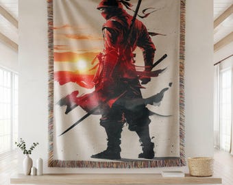 Op de afbeelding: Een geweven sprei met een illustratie van een rode ninja-krijger tegen een zonsondergang. De ninja, in een rode outfit en masker, wordt getoond met zwaarden. De deken heeft een gefranjerde rand.