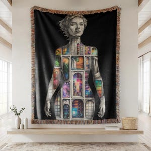 Puede incluir: Manta tejida negra con una ilustraci&oacute;n detallada de la forma de una mujer, con una serie de escenas de ventanas coloridas dentro de su silueta. La manta tiene un borde con flecos y se exhibe en una pared.