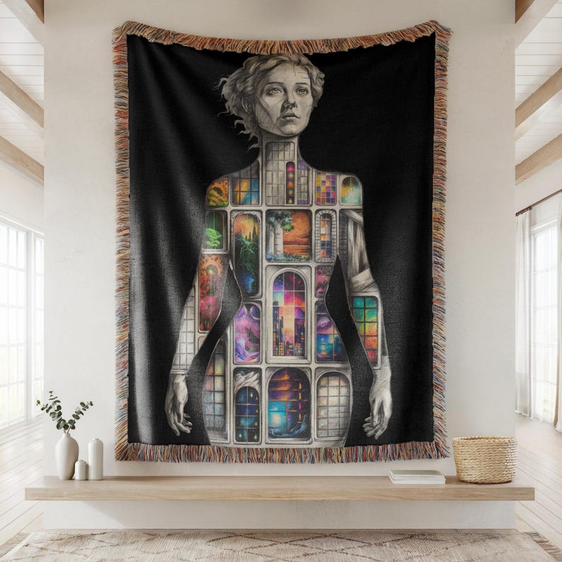 Puede incluir: Manta tejida negra con una ilustraci&oacute;n detallada de la forma de una mujer, con una serie de escenas de ventanas coloridas dentro de su silueta. La manta tiene un borde con flecos y se exhibe en una pared.