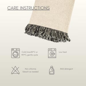 Puede incluir: Una manta de color crema con flecos negros y blancos. La imagen incluye instrucciones de cuidado: lavar en fr&iacute;o (m&aacute;x. 30&deg;C), baja temperatura, lej&iacute;a sin cloro seg&uacute;n sea necesario y detergente suave.