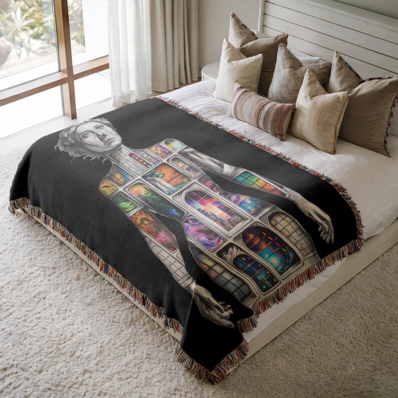 Puede incluir: Manta negra con una ilustraci&oacute;n detallada de una persona con un dise&ntilde;o de ventana. Las ventanas est&aacute;n llenas de arte abstracto colorido. La manta tiene un borde con flecos y se muestra en una cama con almohadas.