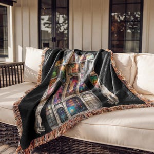 Puede incluir: Manta negra con un dise&ntilde;o art&iacute;stico y colorido de ventanas y una figura. La manta tiene un borde con flecos en tonos marrones y beige. La manta est&aacute; sobre un sof&aacute; blanco.