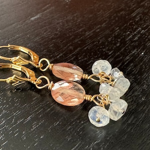 May include: Gold earrings with a pink and white gemstone dangle. The earrings have a leverback closure.