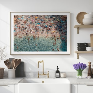 May include: An aerial photograph of a crowded beach with people swimming and sunbathing in the turquoise water. The beach is lined with colorful umbrellas and beach chairs.