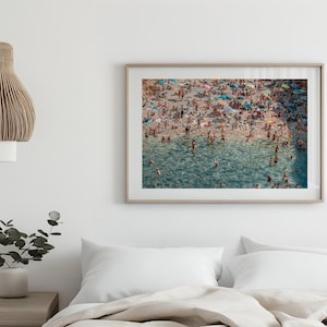 May include: An aerial view of a crowded beach with people swimming and sunbathing in the turquoise water. The beach is covered in colorful umbrellas and towels.