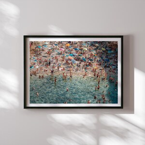 May include: An aerial view of a crowded beach with people swimming and sunbathing in the turquoise water. The beach is covered in colorful umbrellas and beach towels.