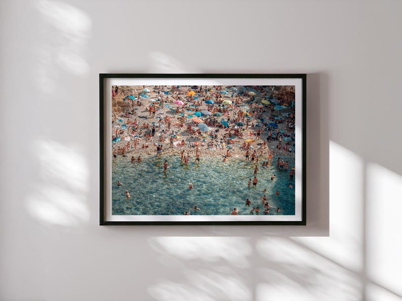 May include: An aerial view of a crowded beach with people swimming and sunbathing in the turquoise water. The beach is covered in colorful umbrellas and beach towels.