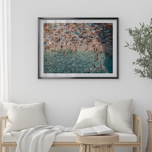 May include: An aerial view of a crowded beach with people swimming and sunbathing in the turquoise water. The beach is covered in colorful umbrellas and towels.
