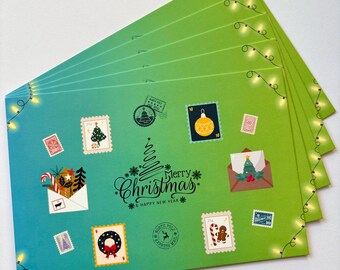 May include: A stack of Christmas-themed greeting cards with a gradient blue to green background. The cards feature festive stamps, a Christmas tree design, and the text "Merry Christmas & Happy New Year". String lights adorn the edges.