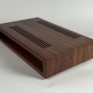 May include: A dark brown wooden coffee table with a rectangular top and a shelf underneath. The top has a series of parallel grooves cut into it.