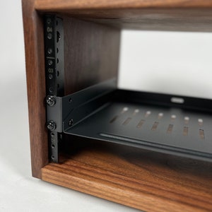 May include: A wooden rack with a black metal shelf. The rack has a series of holes on the side for mounting equipment. The shelf is designed to hold electronic equipment.